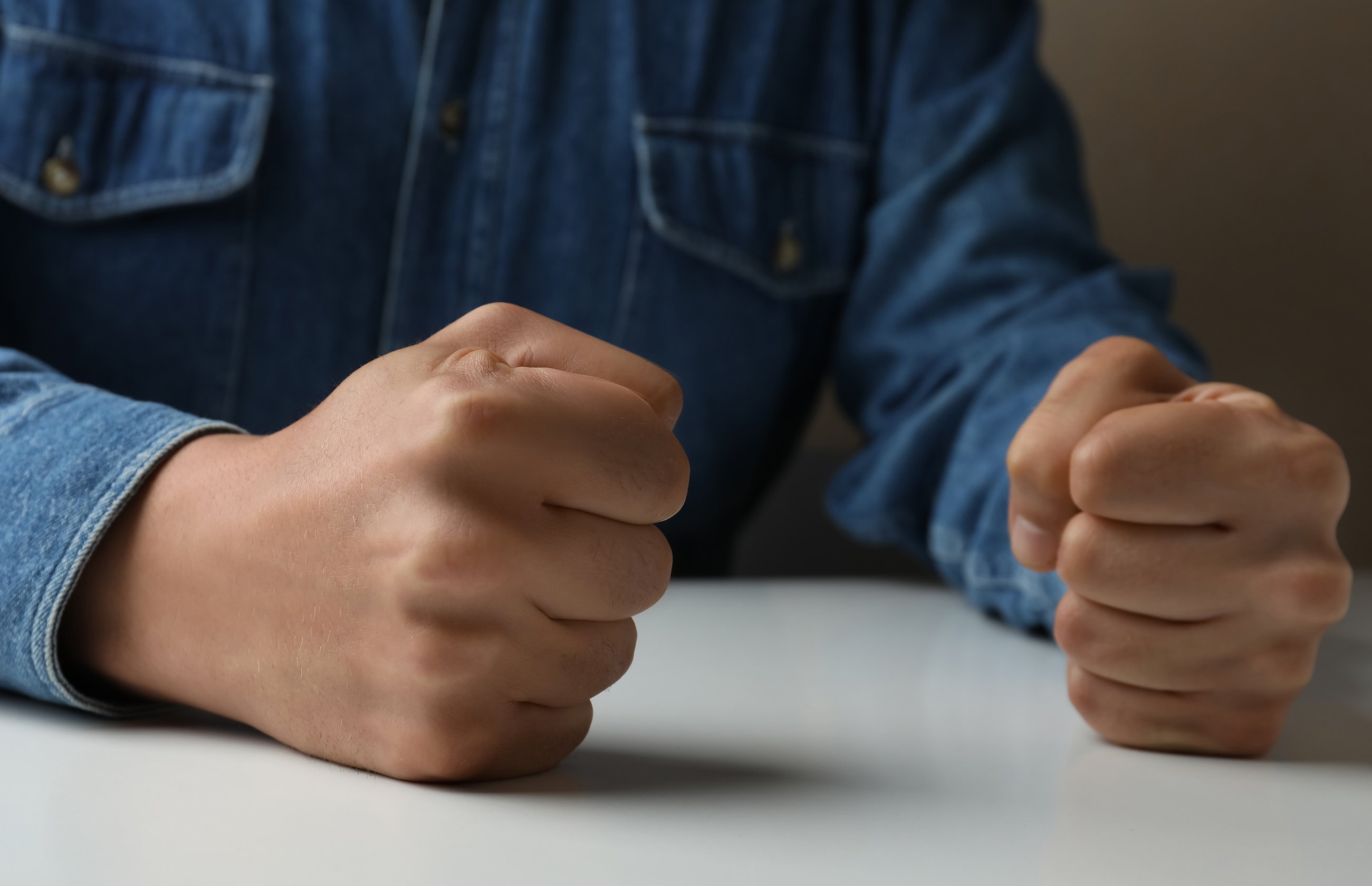 Man Clenching Fists at Table While Restraining Anger, Closeup